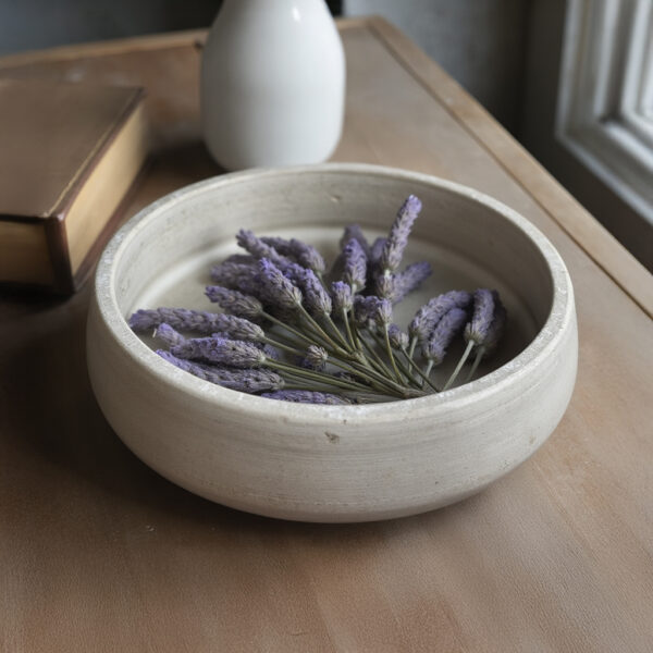 Travertine stone bowl in bathroom setting holding rolled white towels as vanity accessory